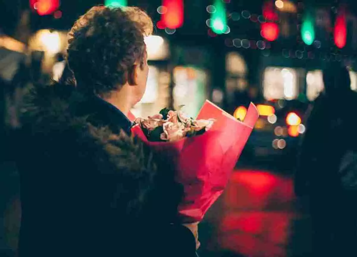 A man waiting on the street with a bunch of flowers in his hands