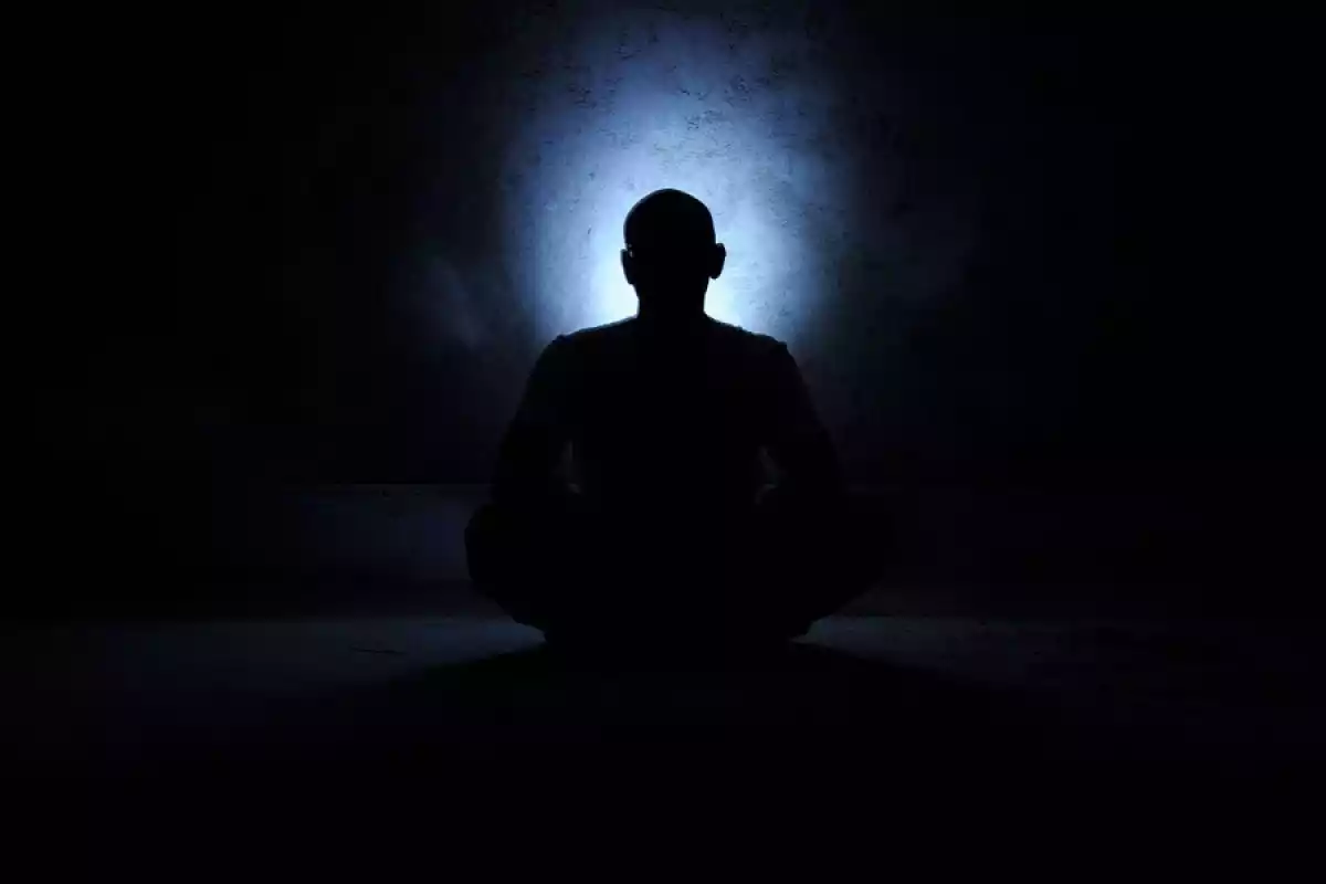 hombre sentado meditando en la oscuridad